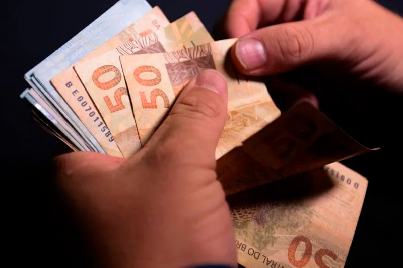 O governo federal enviou ao Congresso, nesta quarta-feira (15), o Projeto de Lei de Diretrizes Orçamentárias (PLDO) de 2027, com proposta de salário mínimo de R$ 1.717. O valor representa um aumento de R$ 96 (5,9%), em relação ao mínimo de 2026, que é de R$ 1.621. O aumento segue a política de valorização do mínimo, que é um dos pilares do terceiro mandato de Lula. O aumento real, ou seja, acima da inflação, era uma promessa de campanha do petista, sob a justificativa de que a medida aumenta o poder de compra das famílias. A política de aumento do mínimo se baseia em um índice que combina a inflação do ano anterior e a variação positiva do Produto Interno Bruto (PIB), que é a soma de toda a riqueza produzida no país, de dois anos anteriores, a partir de 1º de janeiro. Além dos trabalhadores, também são beneficiados pelo aumento do salário mínimo os aposentados, pensionistas e beneficiários de benefícios sociais. O PLDO enviado ao Congresso Nacional será analisado pela Comissão Mista de Orçamento (CMO) e pelo plenário da Câmara dos Deputados e do Senado Federal. Mesmo com esse número apresentado na LDO, o valor do piso salarial de 2027 ainda pode ser alterado. Uma nova avaliação será encaminhada com a proposta orçamentária, que deverá ser apresentada até o dia 31 de agosto, e o valor final só será conhecido em dezembro deste ano, quando será divulgado o Índice Nacional de Preços ao Consumidor (INPC) de novembro. As diretrizes do orçamento propostas pelo governo preveem, ainda, um superávit primário de 0,5% do PIB em 2027, o equivalente a R$ 73,2 bilhões. A margem de tolerância é de 0,25% para cima ou para baixo, sendo que o piso de superávit é de R$ 36,6 bilhões e o teto é de R$ 109,8 bilhões. Apesar disso, o governo prevê que R$ 65 bilhões serão retirados do cálculo do resultado primário. Os descontos são referentes a gastos com precatórios, defesa, saúde e educação. Além disso, o texto prevê que a Dívida Bruta do Governo Geral (DBGG) deve chegar a 83,4% do PIB no próximo ano.